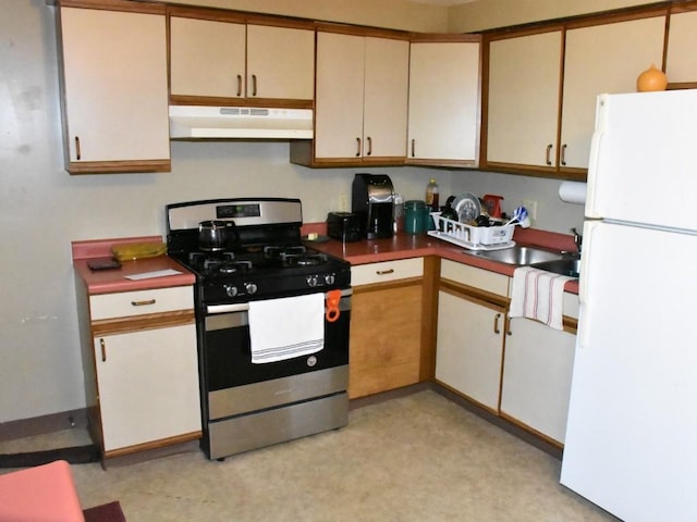 kitchen featuring under cabinet range hood, dark countertops, stainless steel gas range oven, and freestanding refrigerator