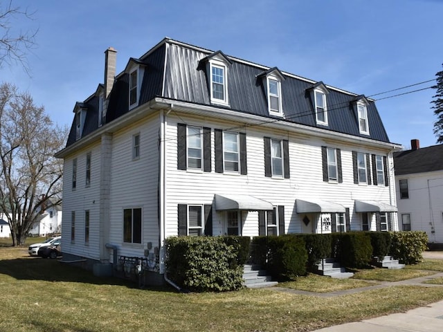 view of front of property featuring a front yard, mansard roof, metal roof, and a chimney