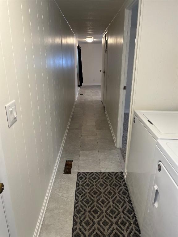 hallway featuring light tile patterned flooring, washing machine and dryer, and wood walls