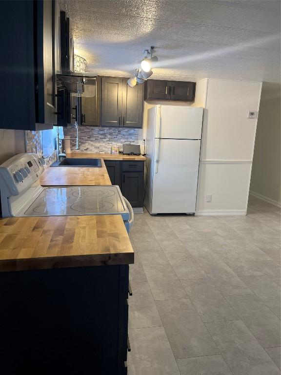 kitchen with white refrigerator, sink, range with electric cooktop, a textured ceiling, and butcher block counters