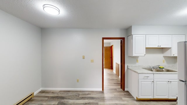 kitchen with white cabinetry, refrigerator, sink, and a baseboard heating unit