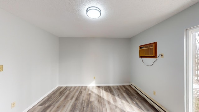 empty room featuring baseboard heating, a wall mounted air conditioner, wood-type flooring, and a textured ceiling