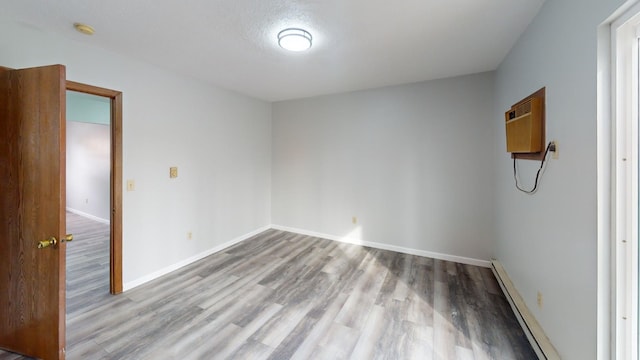 spare room featuring light hardwood / wood-style flooring, a wall mounted AC, and a baseboard radiator