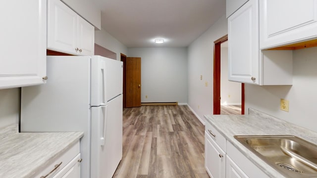 kitchen featuring white refrigerator, light wood-type flooring, sink, and white cabinets