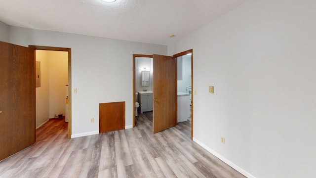 unfurnished bedroom with connected bathroom, electric panel, and light hardwood / wood-style floors