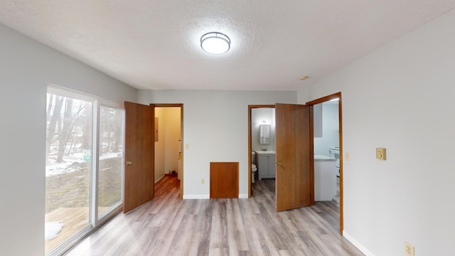 unfurnished bedroom with multiple windows, connected bathroom, a textured ceiling, and light wood-type flooring