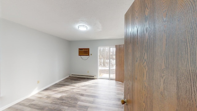 empty room with an AC wall unit, a baseboard heating unit, a textured ceiling, and light hardwood / wood-style flooring