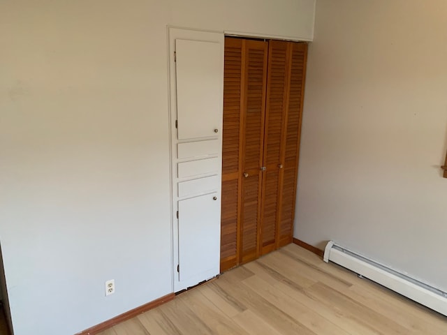 unfurnished bedroom with light wood-type flooring, a baseboard radiator, and a closet