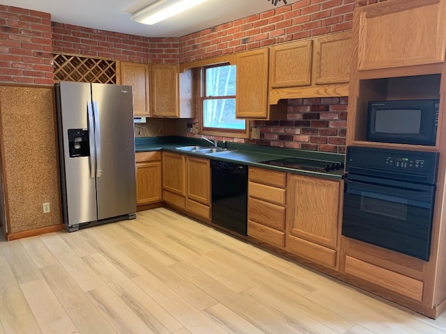 kitchen featuring black appliances, light hardwood / wood-style floors, sink, and brick wall