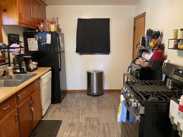 kitchen featuring stainless steel gas range oven, black fridge, dishwasher, and sink