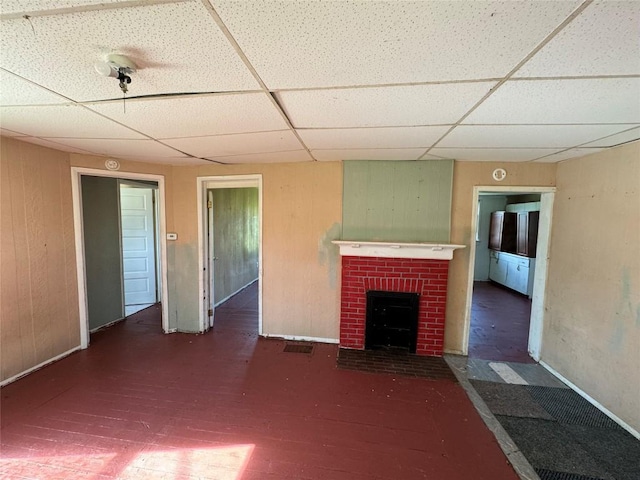 unfurnished living room with a drop ceiling and a brick fireplace