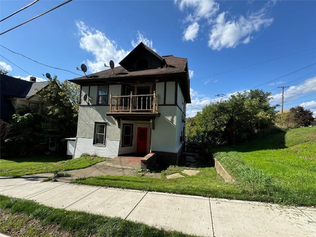 tudor home featuring a balcony and a front lawn