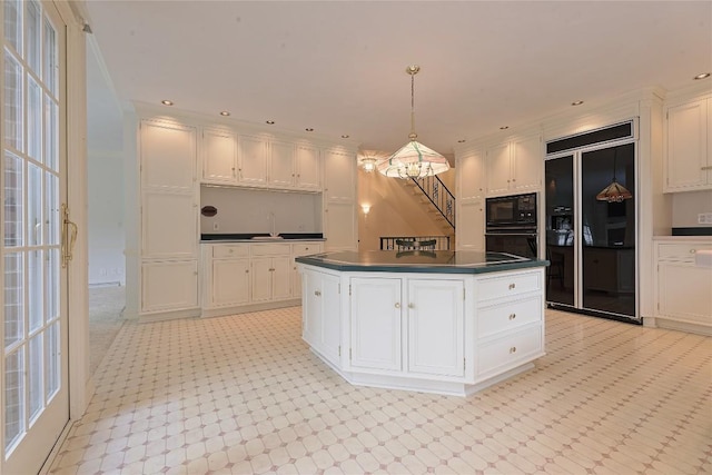 kitchen with a center island, a notable chandelier, pendant lighting, white cabinets, and black appliances