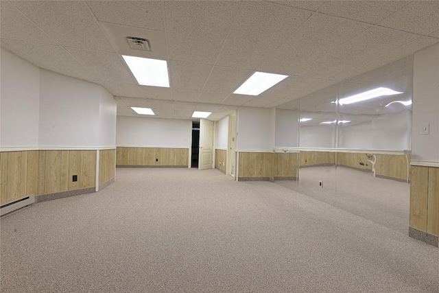 basement with a paneled ceiling, light carpet, and wood walls