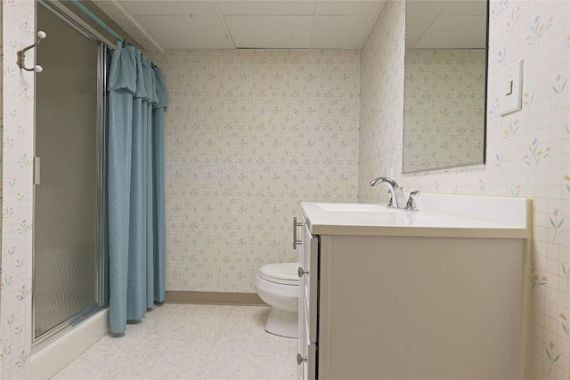 bathroom featuring walk in shower, a drop ceiling, vanity, and toilet