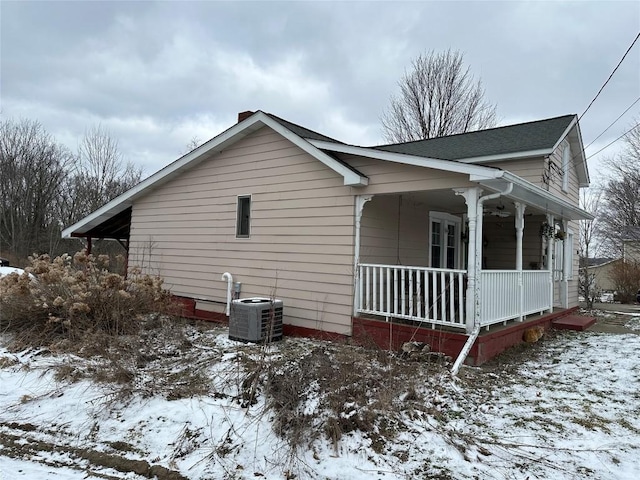 view of snow covered exterior featuring a shingled roof, a porch, and central AC