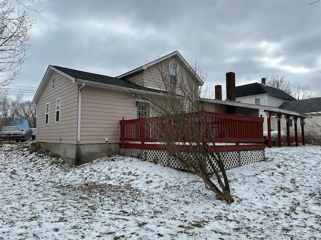 snow covered back of property with a wooden deck