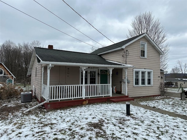 traditional home with a porch, roof with shingles, a chimney, and central AC unit