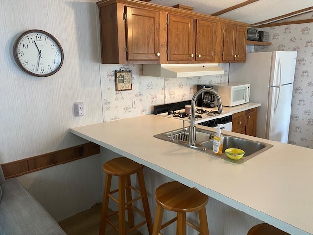 kitchen featuring a kitchen bar, sink, and white appliances