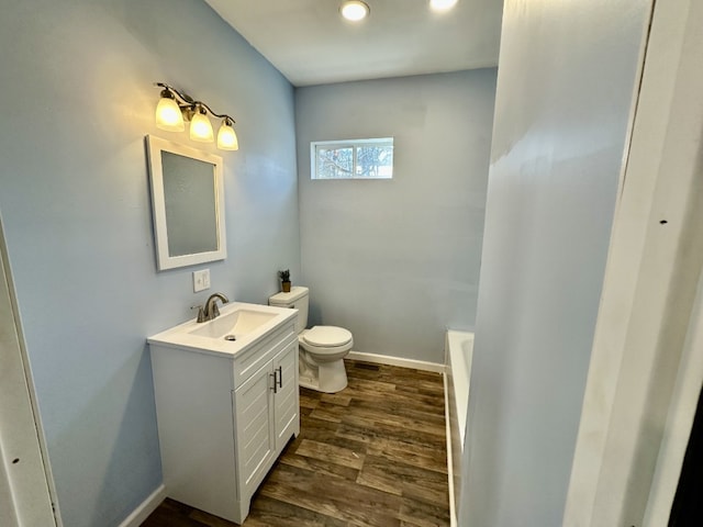 full bath featuring a tub, baseboards, toilet, wood finished floors, and vanity