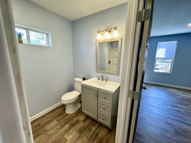 half bathroom featuring toilet, vanity, baseboards, and wood finished floors