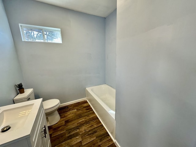 full bath featuring baseboards, toilet, a tub to relax in, wood finished floors, and vanity