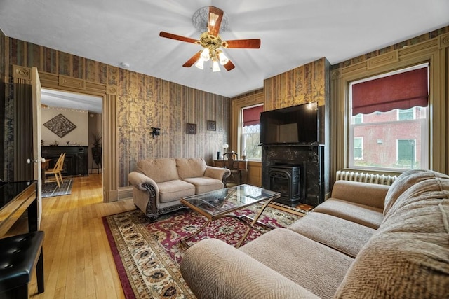 living room featuring a wood stove, ceiling fan, and light wood-type flooring