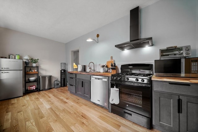 kitchen with sink, wall chimney exhaust hood, stainless steel appliances, wood counters, and light wood-type flooring