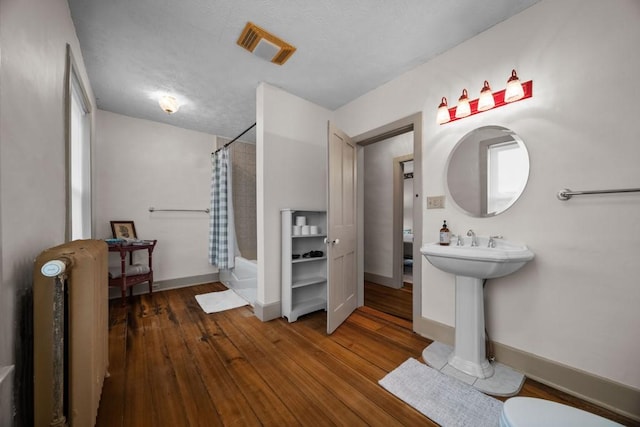 bathroom featuring shower / bath combo, sink, hardwood / wood-style flooring, a textured ceiling, and radiator heating unit