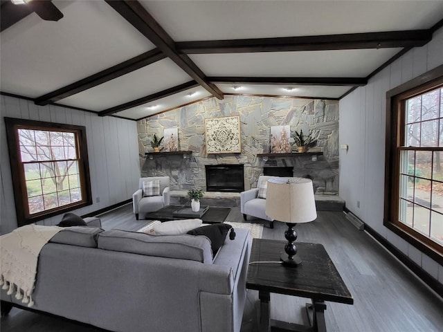 living room featuring hardwood / wood-style floors, vaulted ceiling with beams, and a stone fireplace