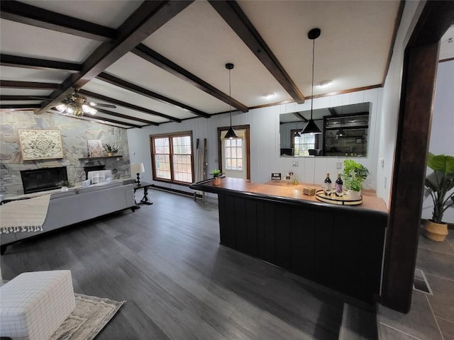 kitchen with dark hardwood / wood-style flooring, ceiling fan, beam ceiling, a stone fireplace, and hanging light fixtures