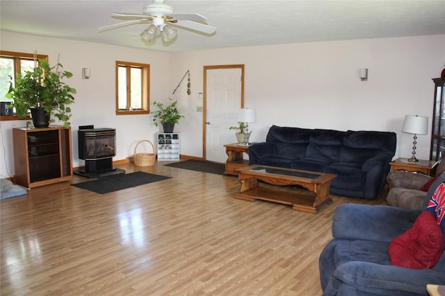 living room with light hardwood / wood-style flooring, a wood stove, and ceiling fan