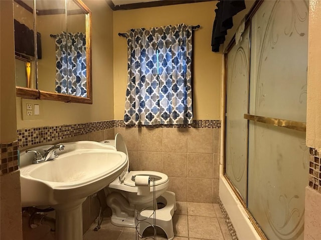 bathroom with tile patterned flooring, combined bath / shower with glass door, tile walls, and toilet