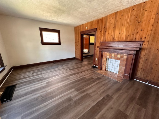 unfurnished living room featuring a textured ceiling, a fireplace, dark wood-type flooring, and wooden walls