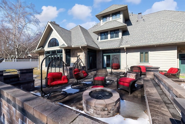 rear view of house featuring a shingled roof, an outdoor living space with a fire pit, a patio, stone siding, and fence