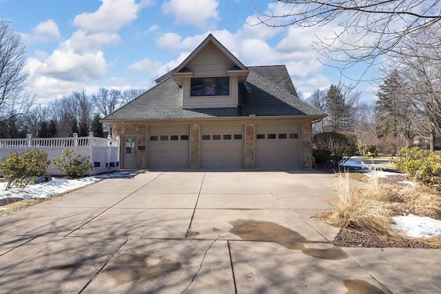 view of home's exterior with an attached garage, fence, driveway, stone siding, and roof with shingles