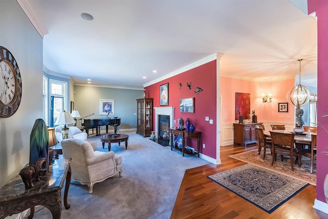 living room featuring crown molding, a fireplace, a notable chandelier, wood finished floors, and baseboards