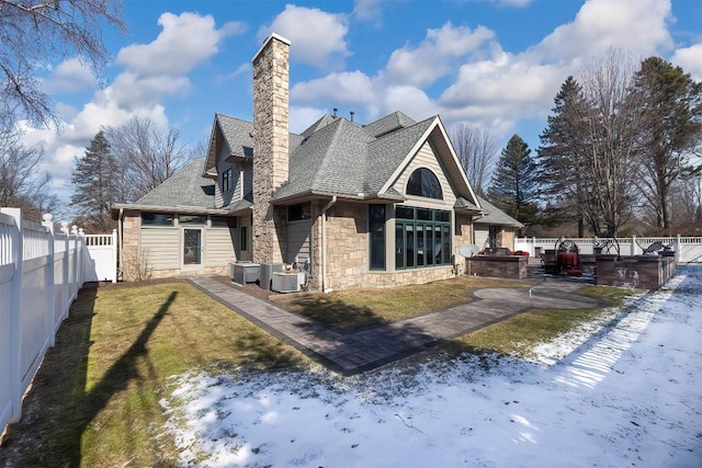 rear view of property with a shingled roof, central AC unit, a lawn, stone siding, and a fenced backyard