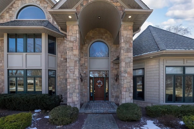 view of exterior entry with a shingled roof and stone siding