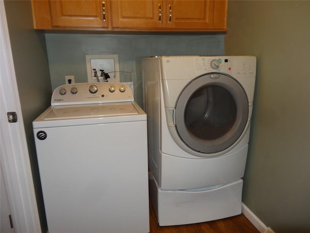 washroom with dark wood-type flooring, washer and clothes dryer, and cabinets