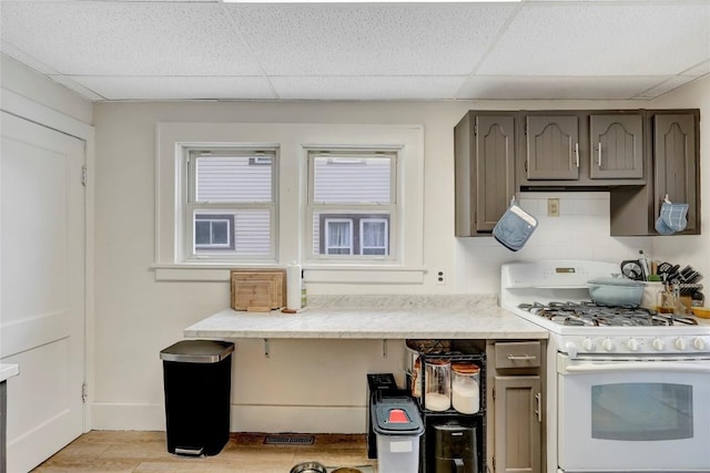 kitchen with gray cabinetry, white gas stove, backsplash, and a drop ceiling