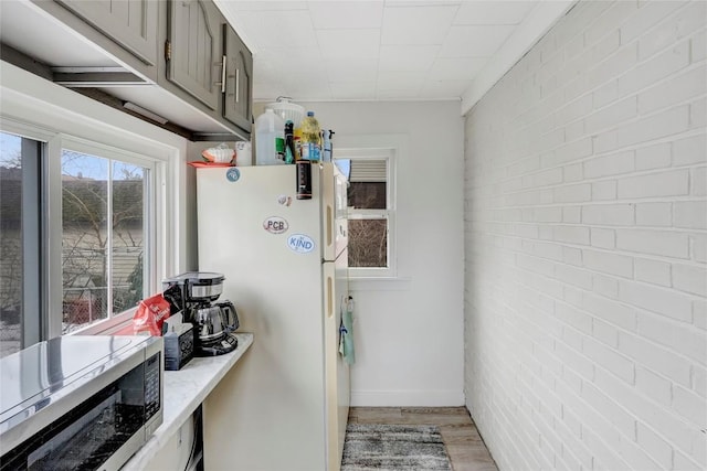 kitchen featuring white refrigerator, brick wall, gray cabinetry, and light wood-type flooring