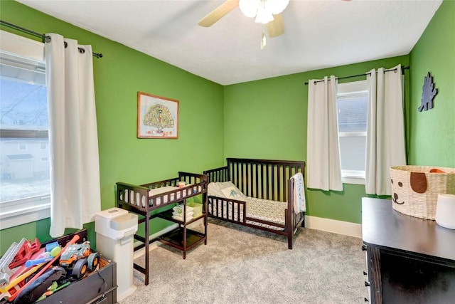 bedroom with light colored carpet, a nursery area, and ceiling fan