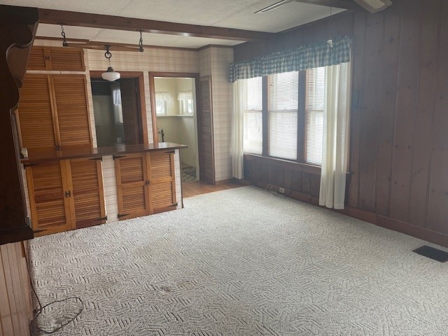 unfurnished living room with beam ceiling, light colored carpet, and wooden walls