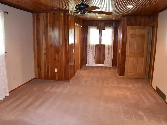 unfurnished room with wood walls, ceiling fan, and light colored carpet