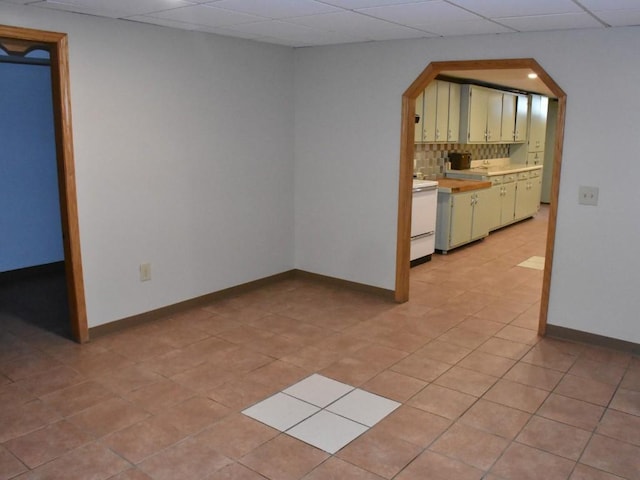 interior space with decorative backsplash, light tile patterned floors, a drop ceiling, and range