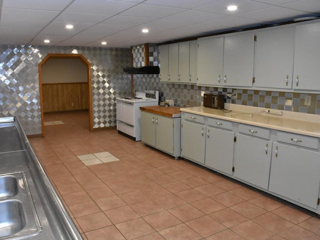 kitchen featuring white range with electric cooktop, wall chimney exhaust hood, decorative backsplash, and light tile patterned floors