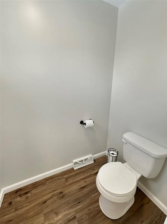 bathroom with baseboards, visible vents, toilet, and wood finished floors