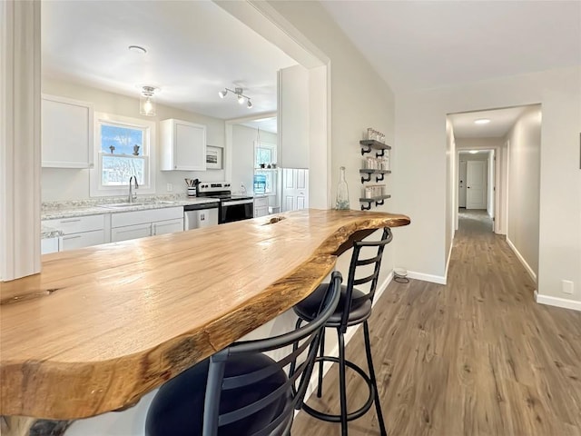 kitchen with stainless steel appliances, light wood-style floors, white cabinets, a sink, and baseboards