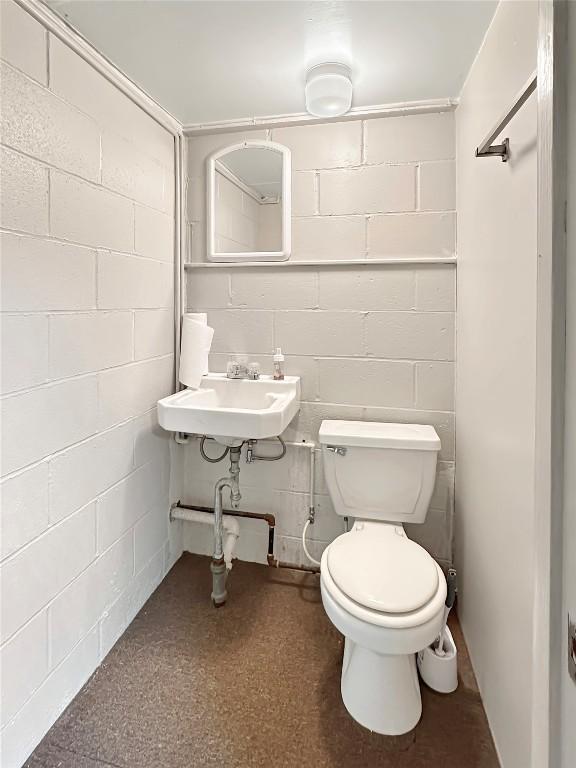 half bath with concrete block wall, a sink, and toilet